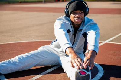 Athlete in grey tracksuit and black beanie stretching on a running track