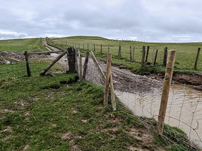 A high wire fence line running alongside a rugged hill trail.