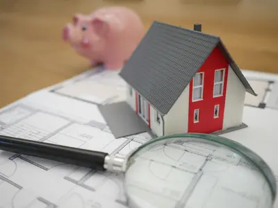 Model house with piggy bank and magnifying glass alongside - 4 Things That Will Make Buying Your First House Go Smoothly