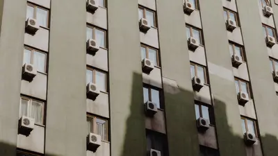 Facade of a city apartment building equipped with air conditioners on each window - Simple Ways to Help Your Air Conditioner Last Longer