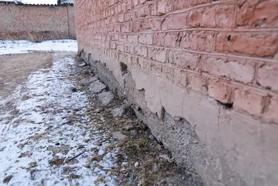 Deteriorating brick wall base showing cracked mortar, exposed masonry and subsidence damage in winter - Keeping Your Home Safe from Water Damage