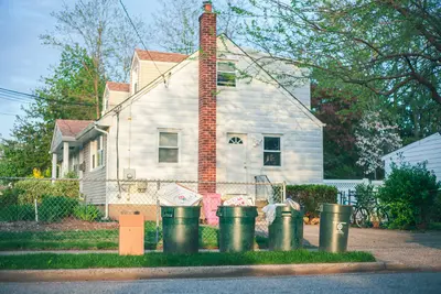 Trash cans in front of a sizeable white house full of household items - How Decluttering Your Home Can Improve Your Wellbeing