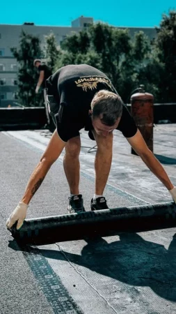 Roofer applying waterproof membrane on a flat roof with a torch, on a sunny rooftop - Is Your Flat Roof Ready for All Seasons?