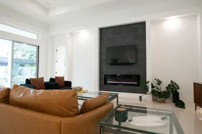 Bright modern living room with tan leather sofa, dark armchairs, and a wall-mounted TV above a linear fireplace with a grey tiled surround - 7 Stunning Ways To Create A Captivating Wall Focal Point In Your Home