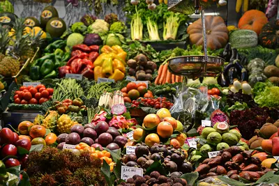 A densely packed market fruit and vegetable stall with hand-labelled signs, featuring peppers, tomatoes, pumpkins, dragon fruit, mangosteen, lychee, salak and other exotic produce alongside an old-fashioned hanging scale - Simple Ways to Get More Fruits and Vegetables Into Your Daily Routine