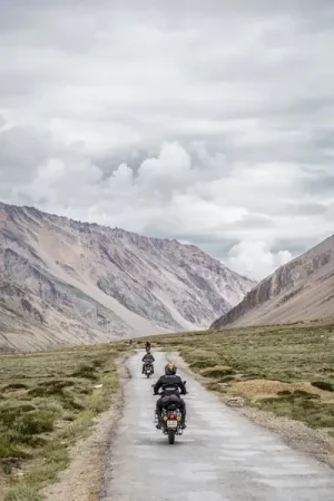 A line of motorcyclists on Royal Enfields rides away down a gravel mountain road, with barren, striated peaks rising under a cloudy sky." - Exploring Wrexham and North Wales by Motorbike