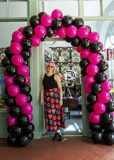 Kerry Fisher under a pink and black balloon arch at Eyecadia – Eyecadia: Bespoke Eyewear, Styling and Colour Analysis in Wrexham
